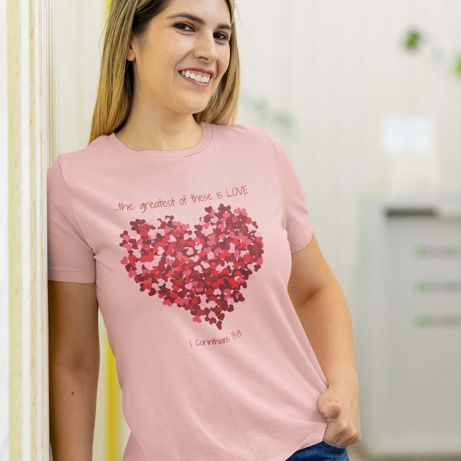 Woman wearing a light pink shirt with a heart design made from small red flowers and the text "the greatest of these is LOVE" from 1 Corinthians 13:13.