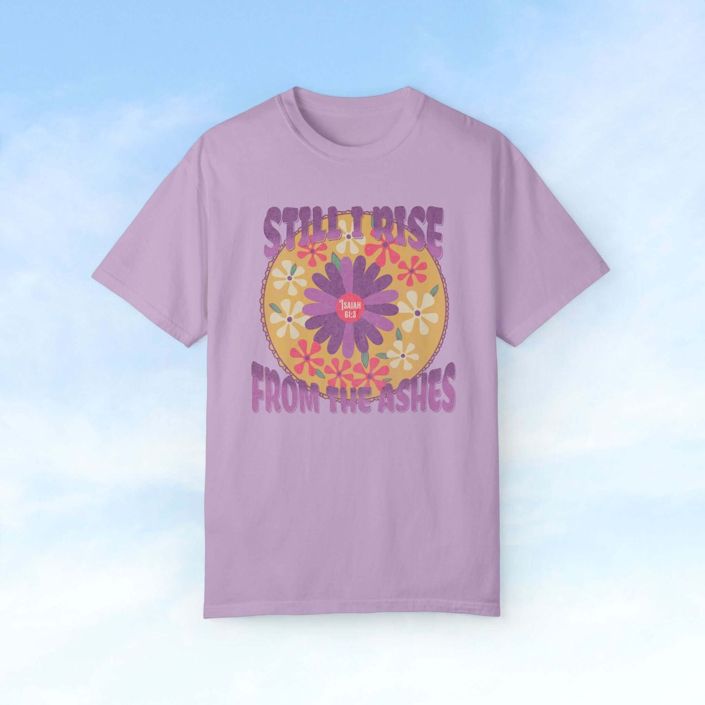 Christian floral shirt with 'Still I Rise From The Ashes' text and boho flower design on a purple t-shirt against a sky background.