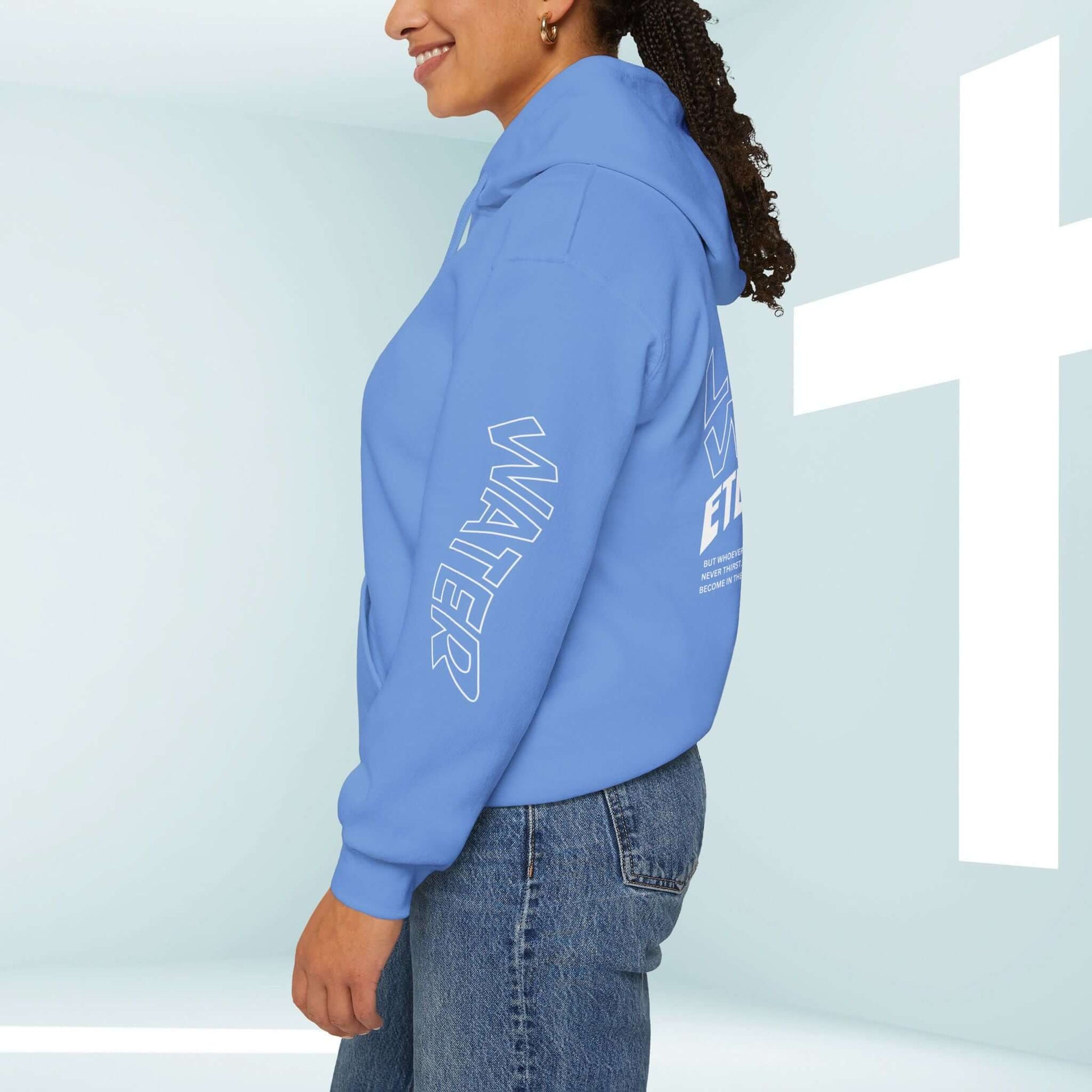 Person wearing a blue Christian hoodie with "Living Water" graphics on sleeves and back, in front of a white cross background