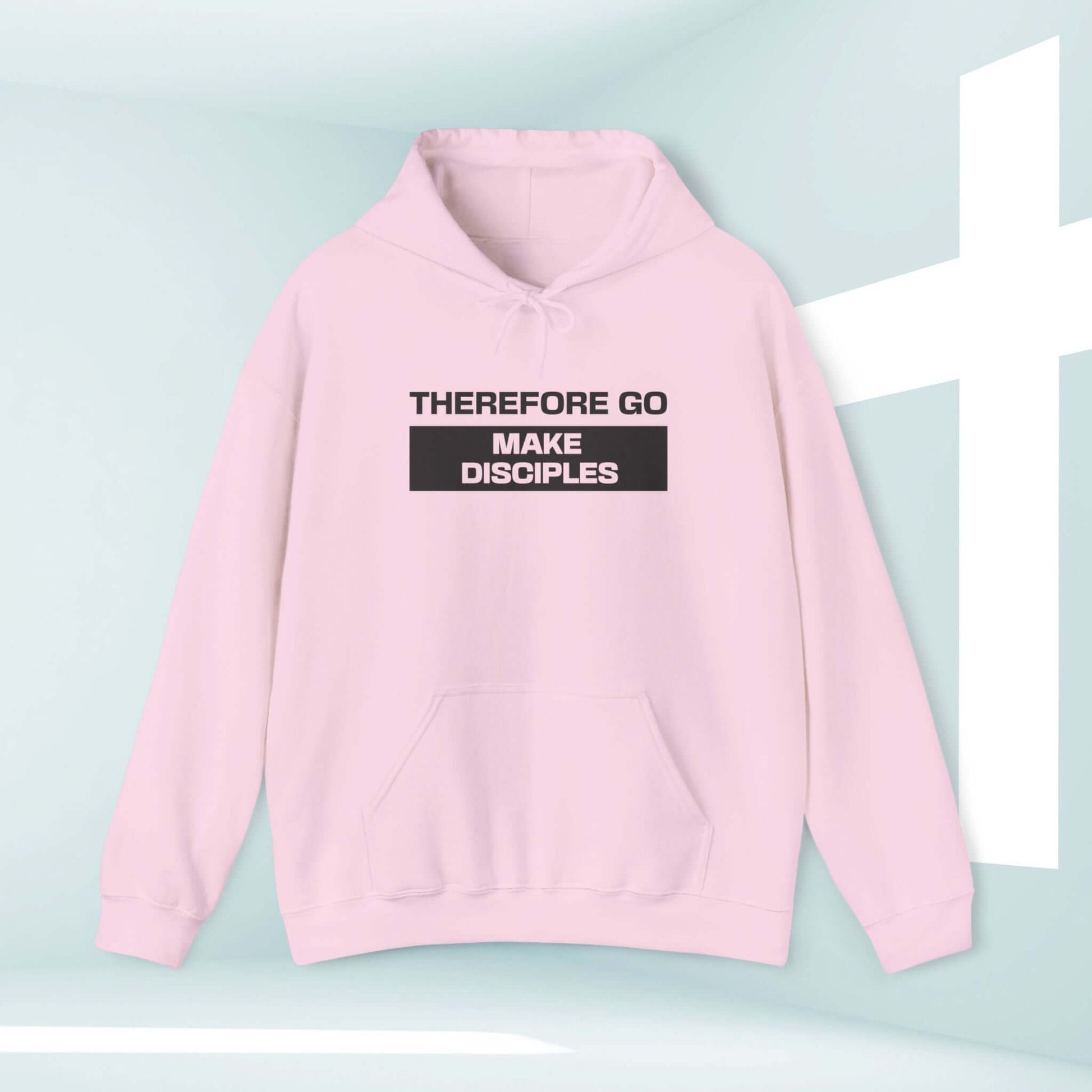 Light pink "Therefore Go And Make Disciples" Bible verse Christian hoodie against a minimalistic background with a white cross.