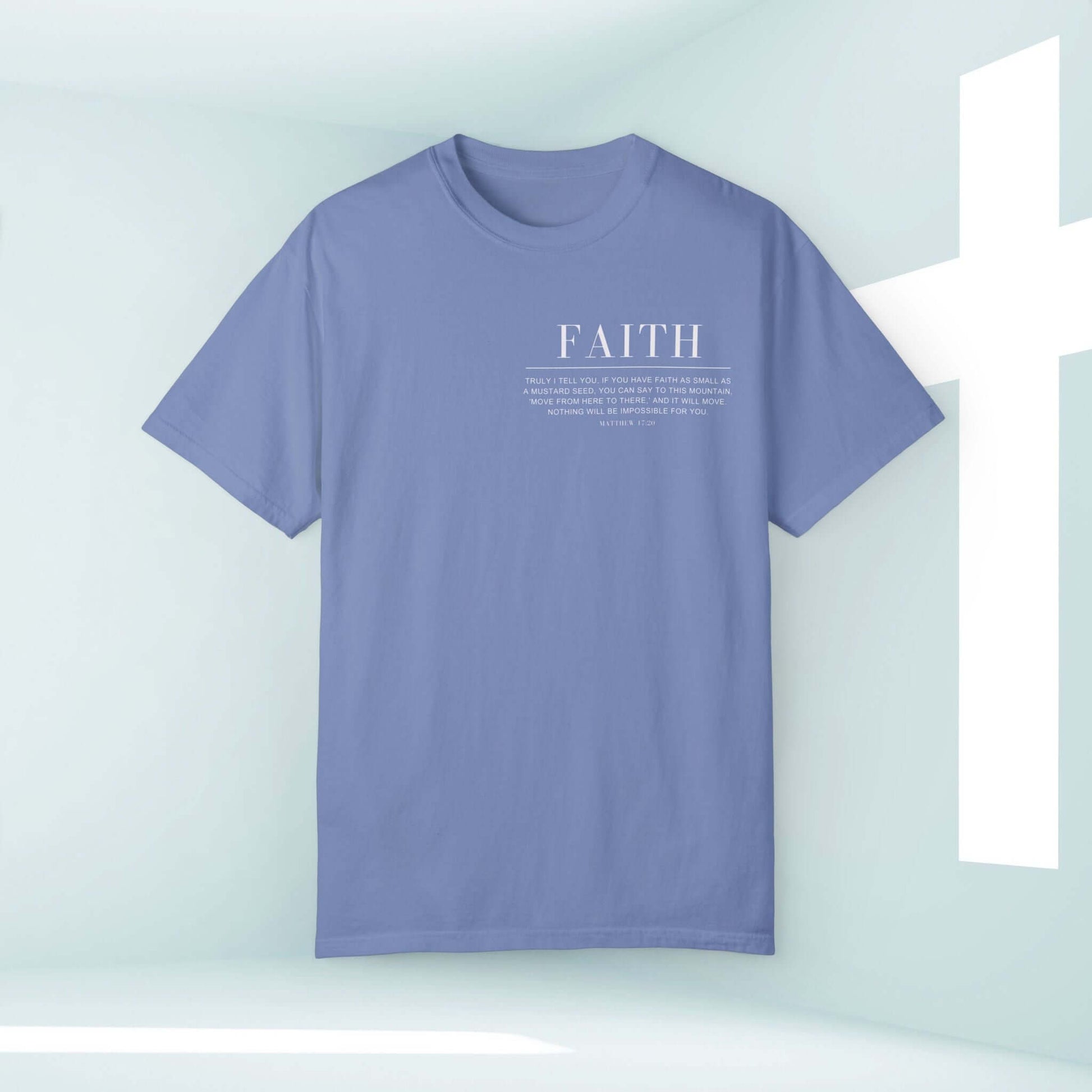 Faith Can Move Mountains Christian t-shirt, faith-based graphic inspirational tee with Bible verse in light blue on display near white cross.