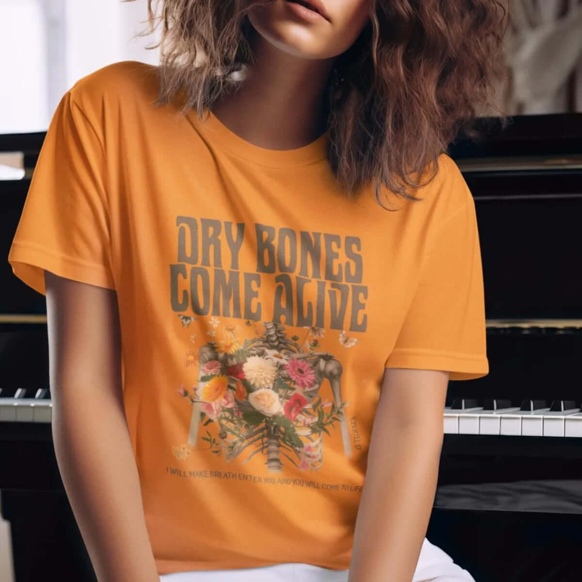 Woman wearing "Dry Bones Come Alive" Christian Halloween t-shirt, featuring a skeleton design, next to a piano.