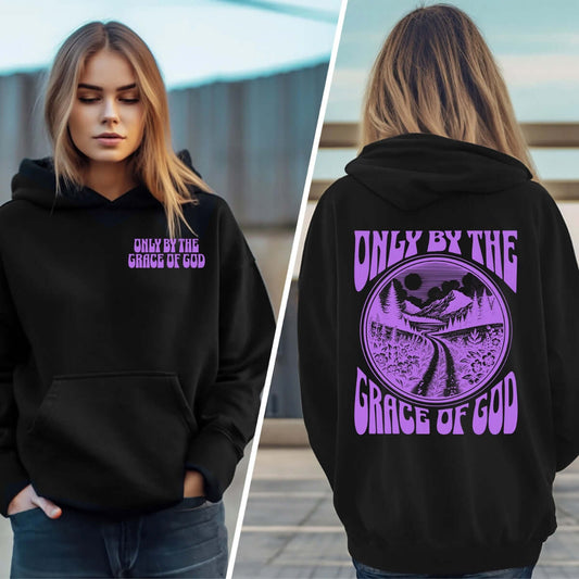 Woman wearing black Christian hoodie with "Only By The Grace Of God" Bible verse in purple text on front and back, faith-based clothing.