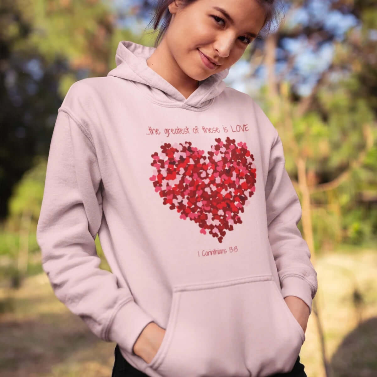 Woman wearing Christian Valentines Day hoodie with heart design and "The Greatest Of These Is Love" Bible verse.