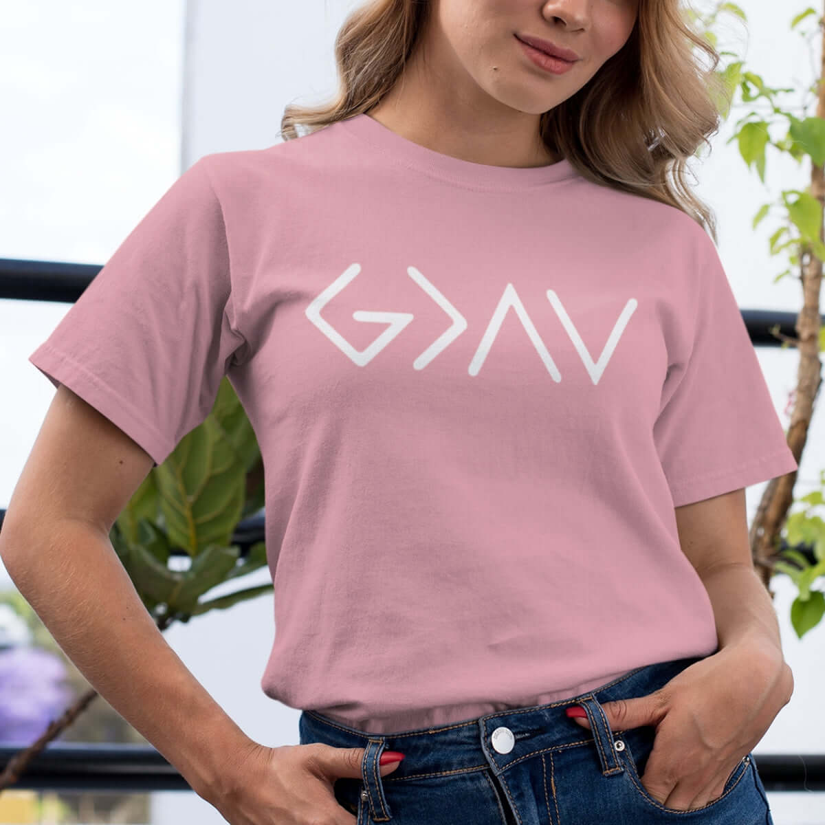 Woman wearing a pink "God Is Greater Than The Highs And The Lows" t-shirt, showcasing Christian faith-based apparel.