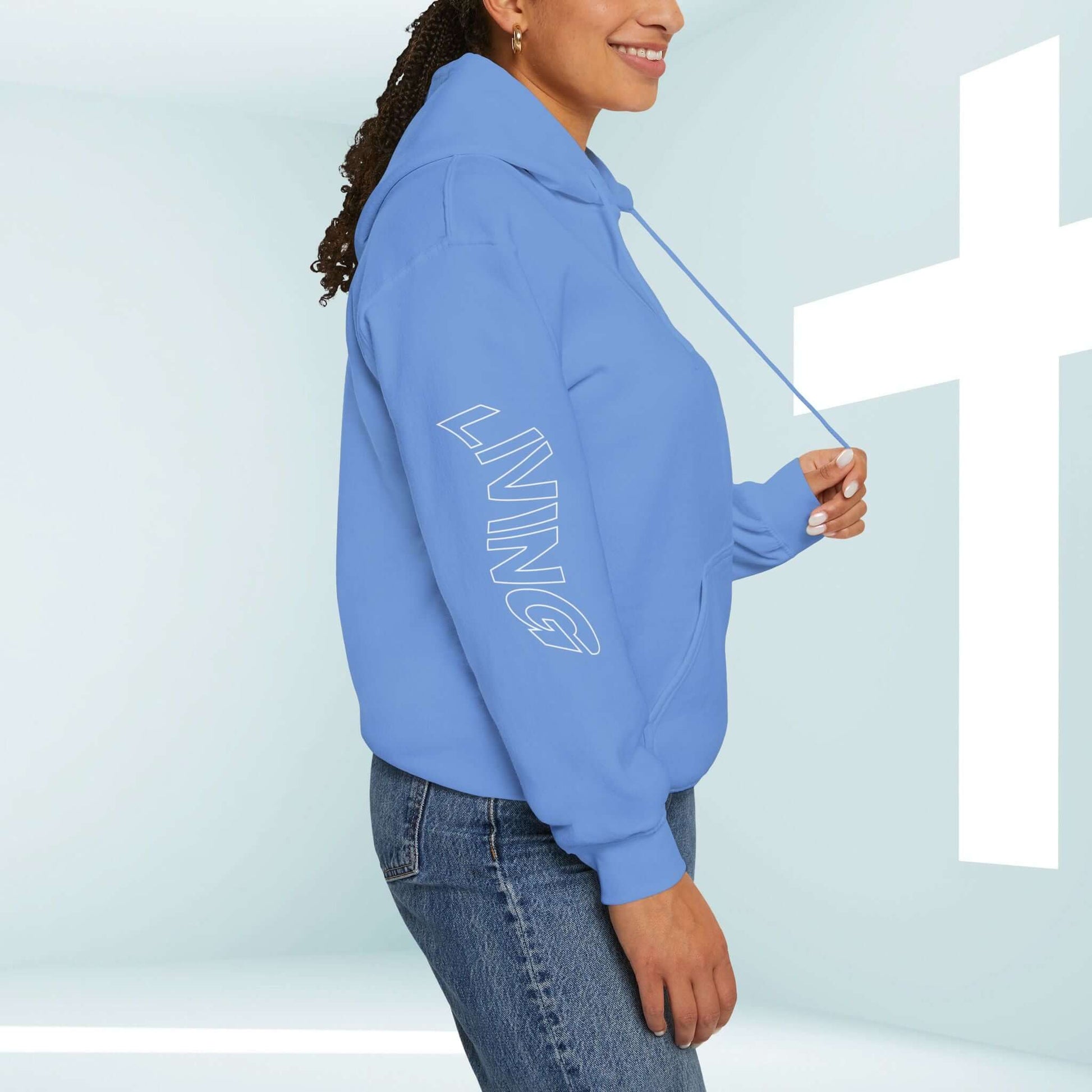 Woman wearing blue Living Water Christian hoodie with faith-based graphic on sleeve against a light background with a white cross in the corner