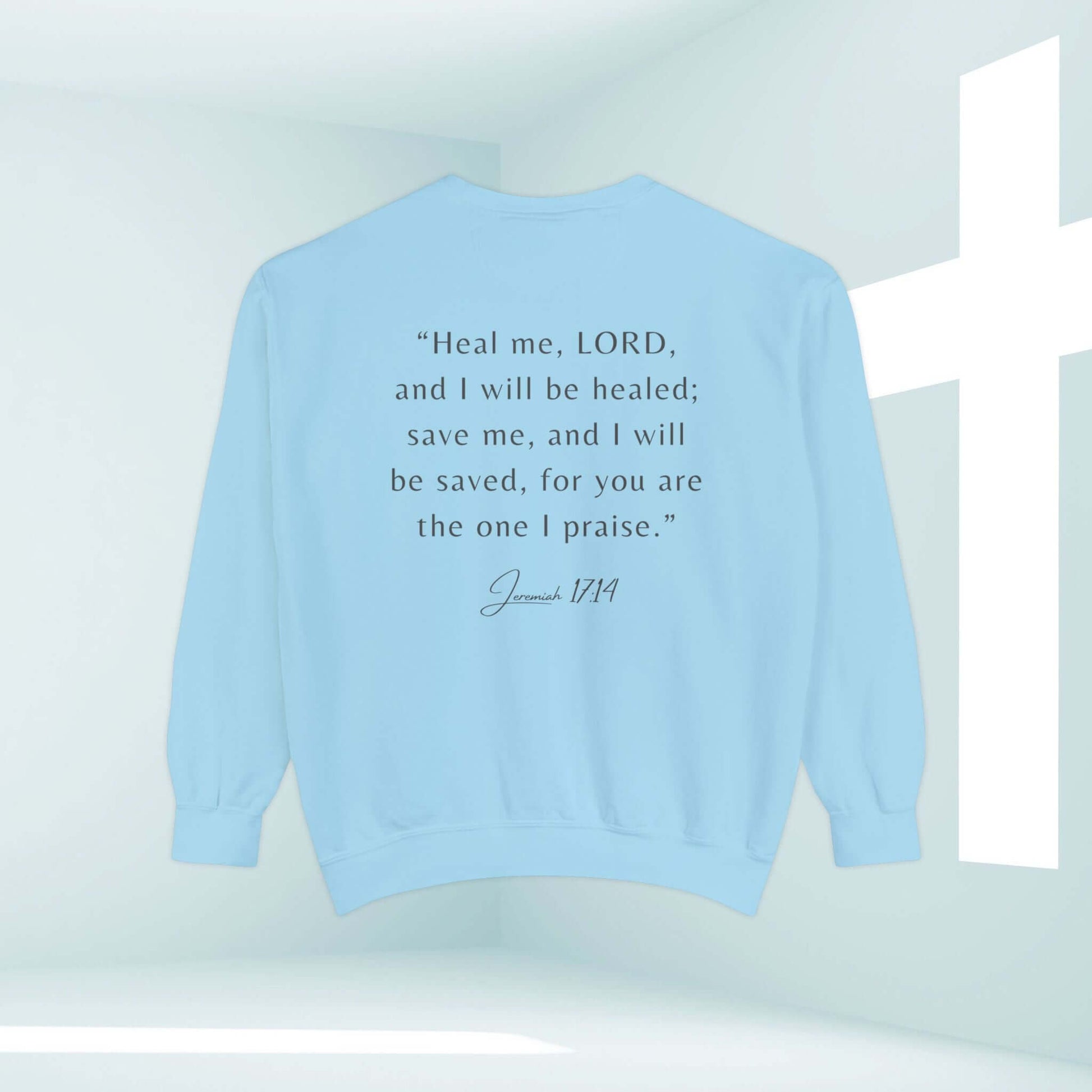 Light blue Christian sweatshirt with Jeremiah 17:14 Bible verse, "Heal me, LORD, and I will be healed; save me, and I will be saved," displayed in a serene room.