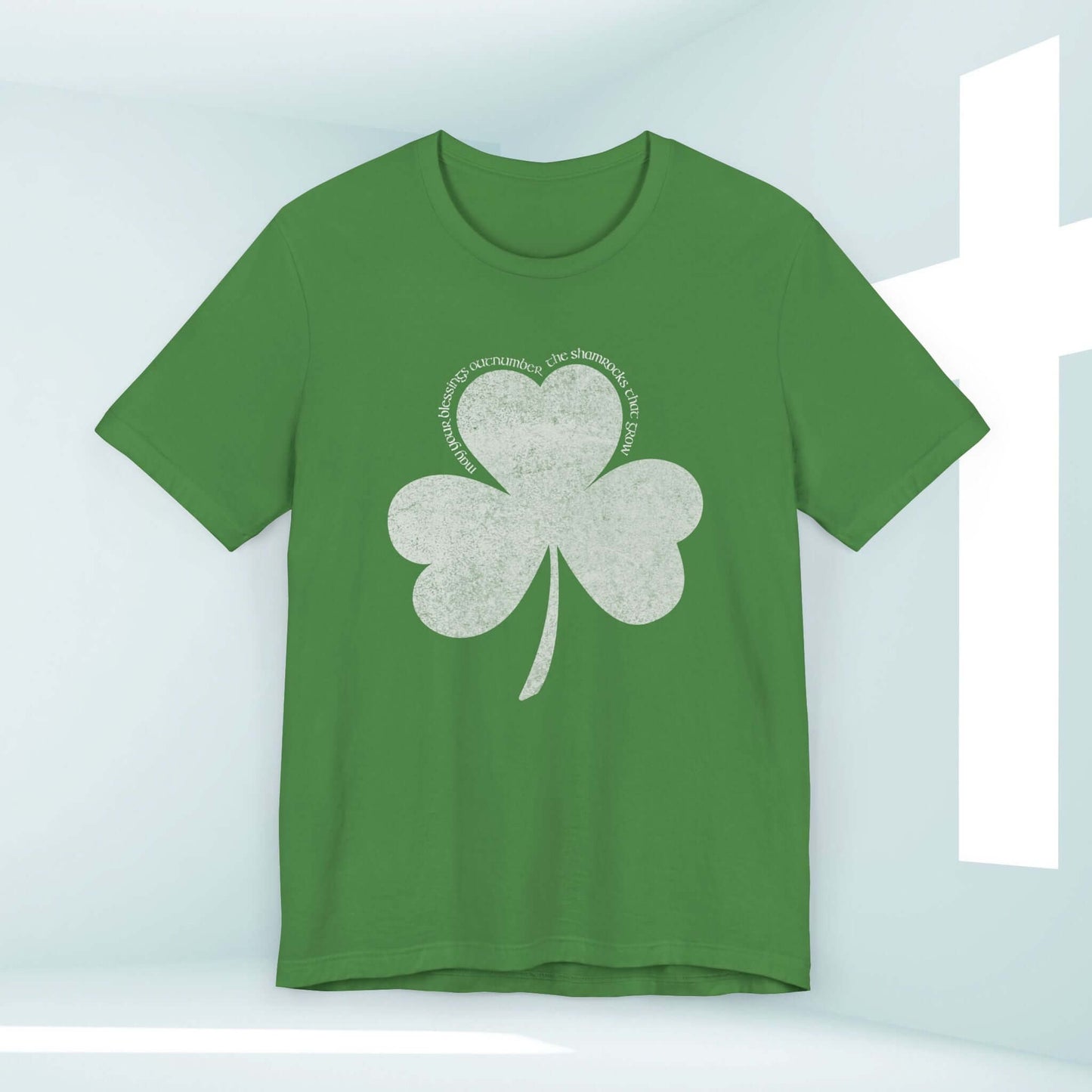 Green St Patrick's Day shirt with shamrock clover design and Christian blessings text in a white room with a cross in the background