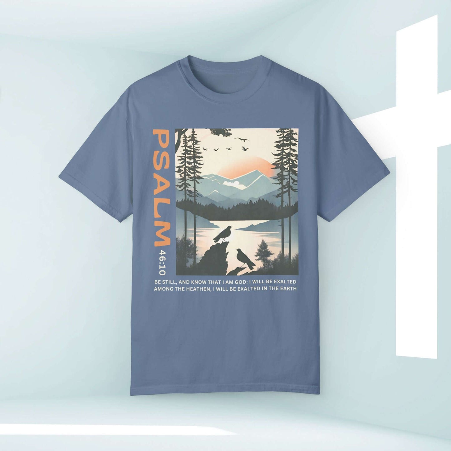 "Christian shirt with 'Peace Be Still' design, featuring birds and Psalm 46:10 scripture in a serene mountain setting"