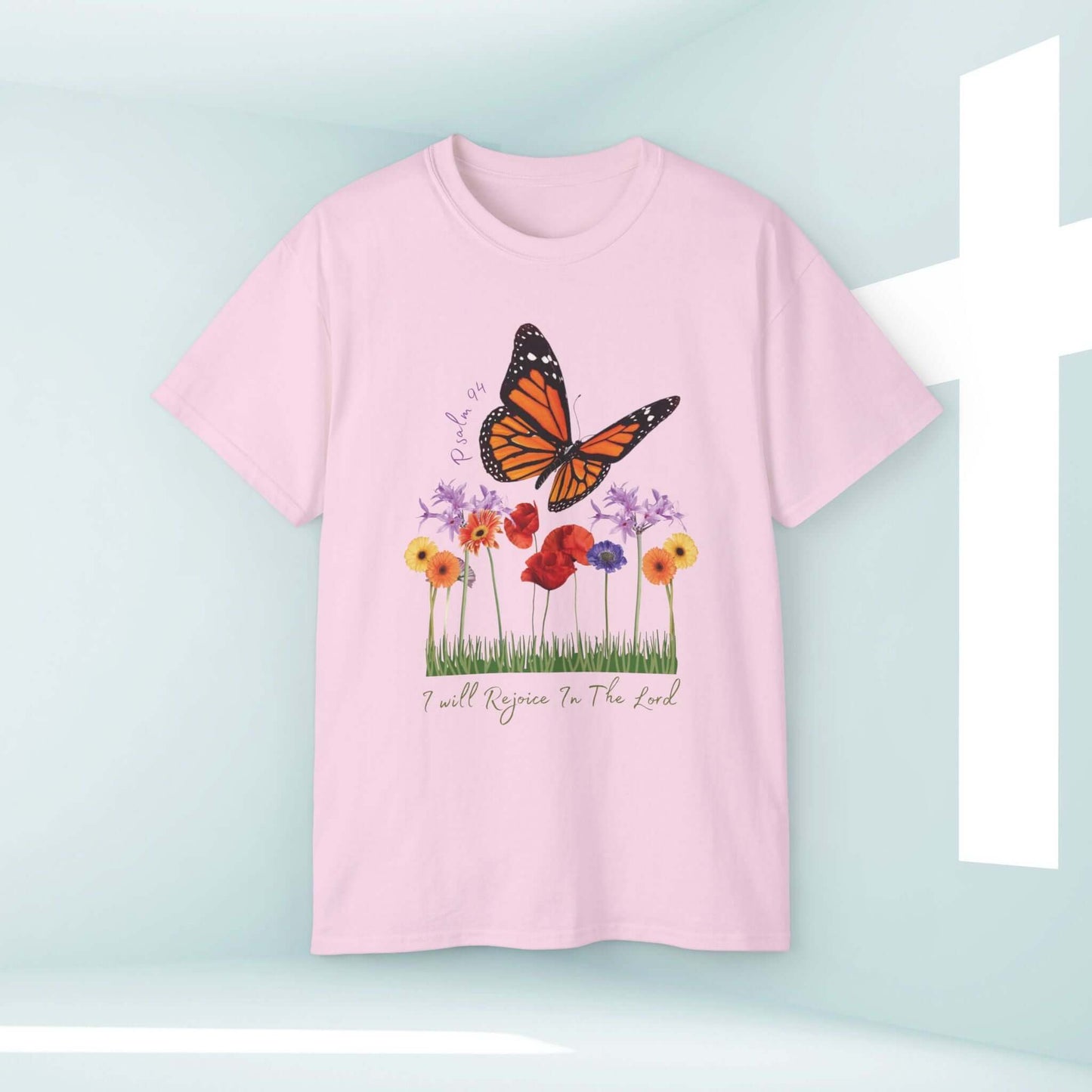 Pink "I Will Rejoice In The Lord" Christian T-shirt with butterfly and floral design in bright room.