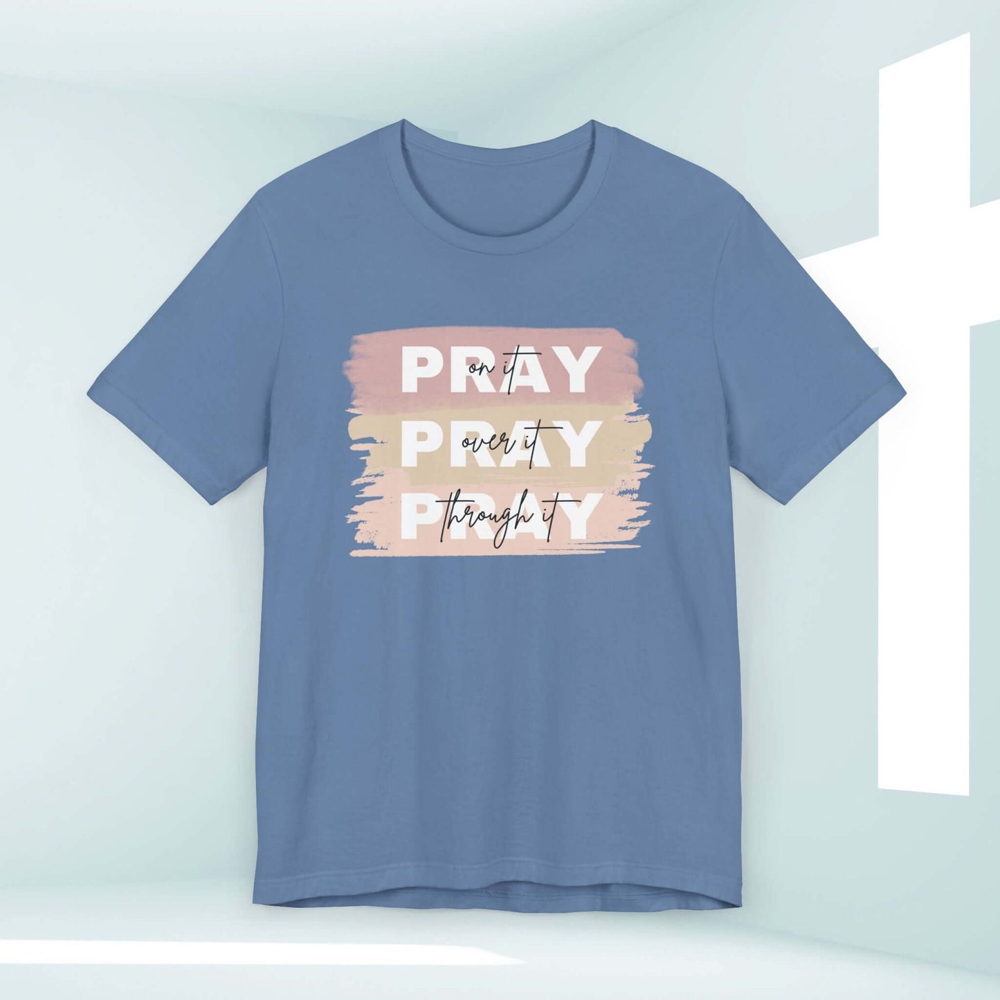 Pray On It, Over It, Through It Christian t-shirt for women in blue with inspirational message against soft background with cross.