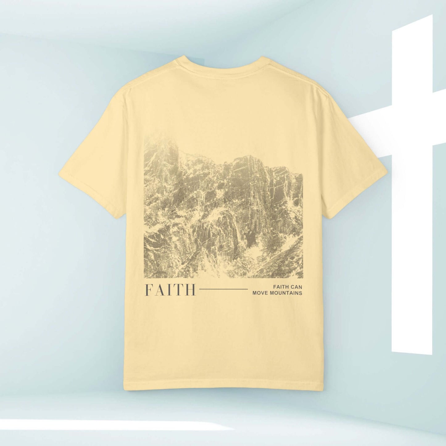 Faith Can Move Mountains Christian shirt with mountain design on the back displayed near a white cross symbol.