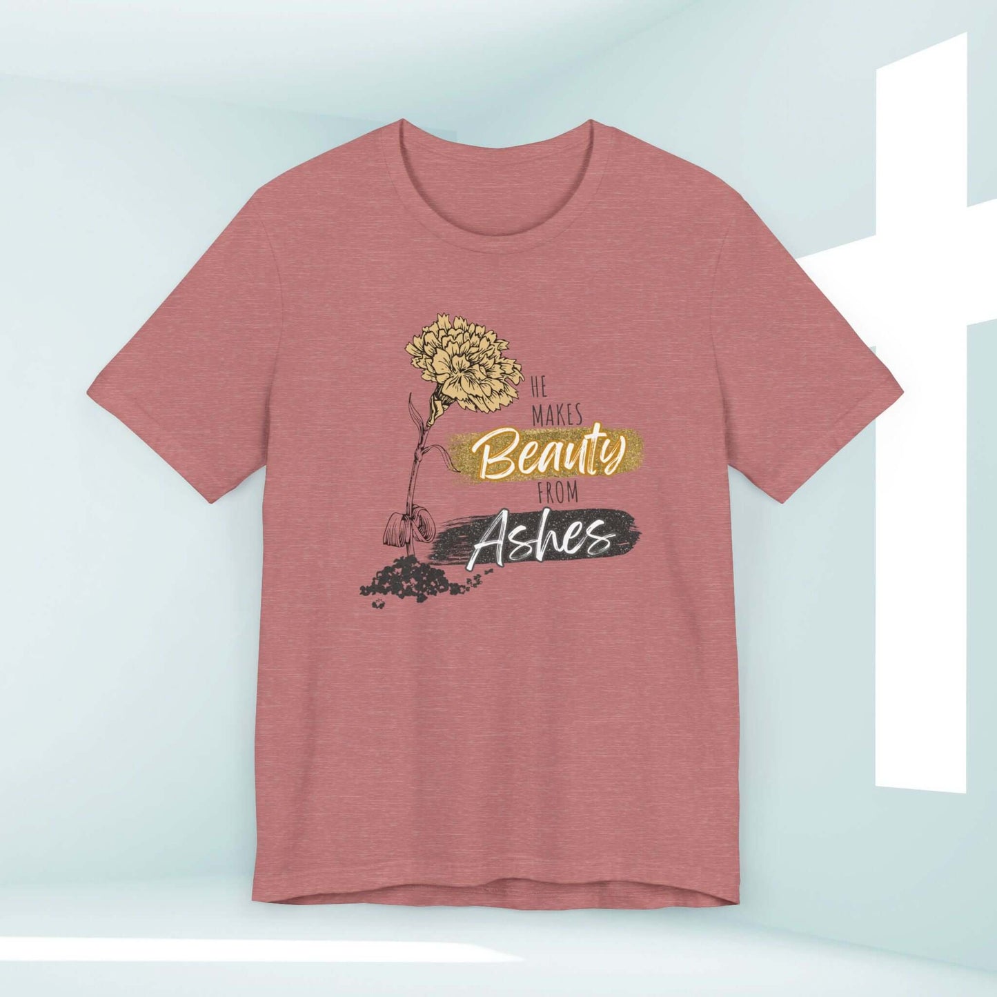 He Makes Beauty From Ashes Women's Christian T-Shirt with Bible Verse in a soft pink color against a cross background