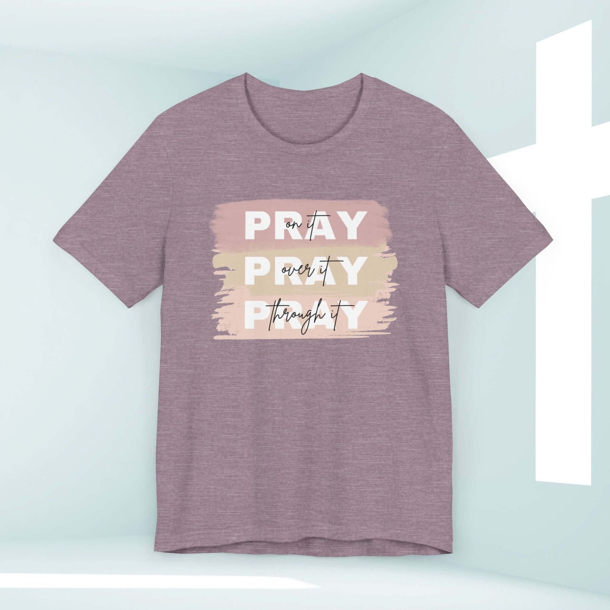 Pray On It, Over It, Through It Christian Women's T-Shirt with Inspirational Message in a Light Purple Color, Hanging Against a Cross Background