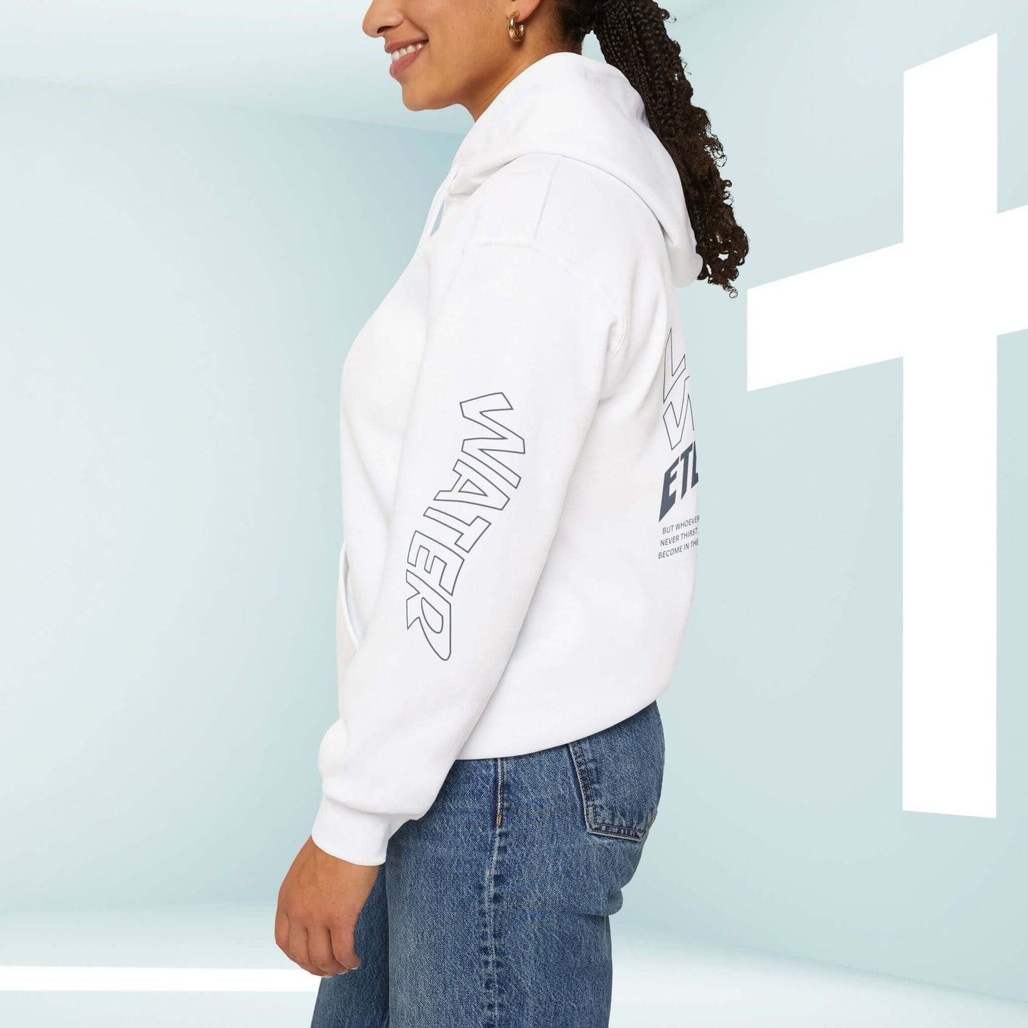 Woman wearing Living Water Eternal Life Christian hoodie with graphics on sleeves and back, standing next to a cross backdrop.