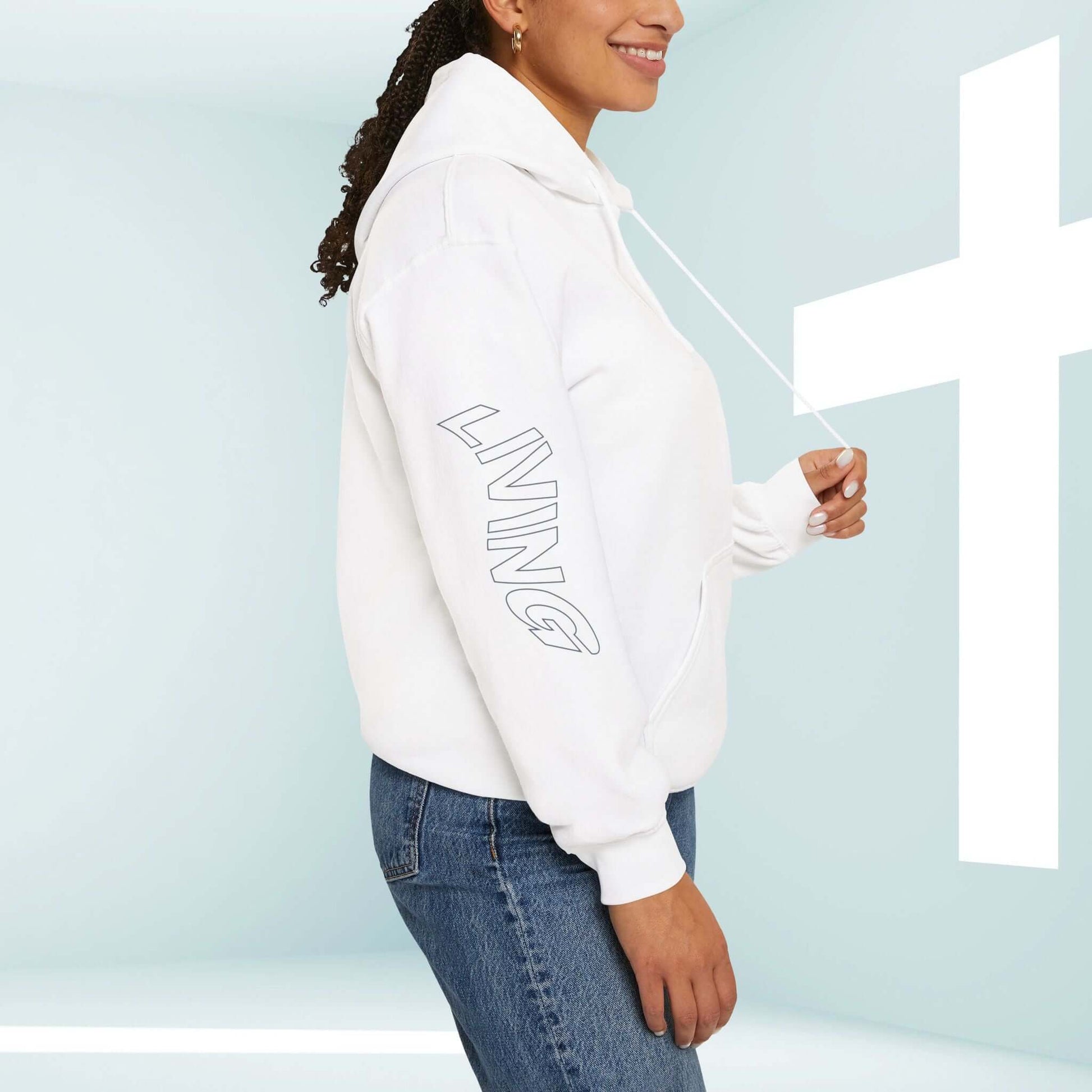 Woman wearing white Christian hoodie with Living Water graphic on sleeve, standing next to a cross, promoting faith-based apparel.