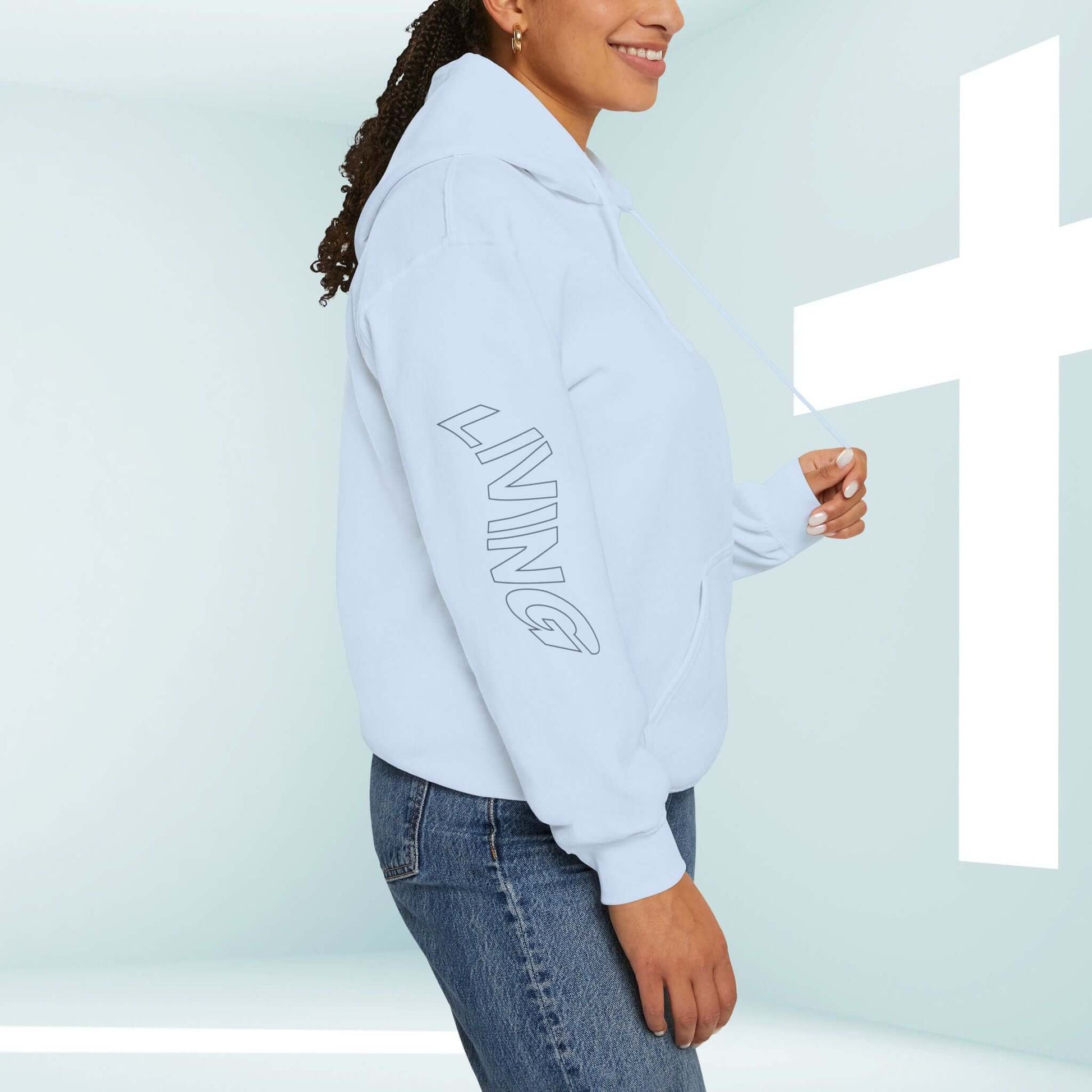 Woman wearing Living Water Eternal Life Christian hoodie featuring sleeve graphics, standing by illuminated cross background