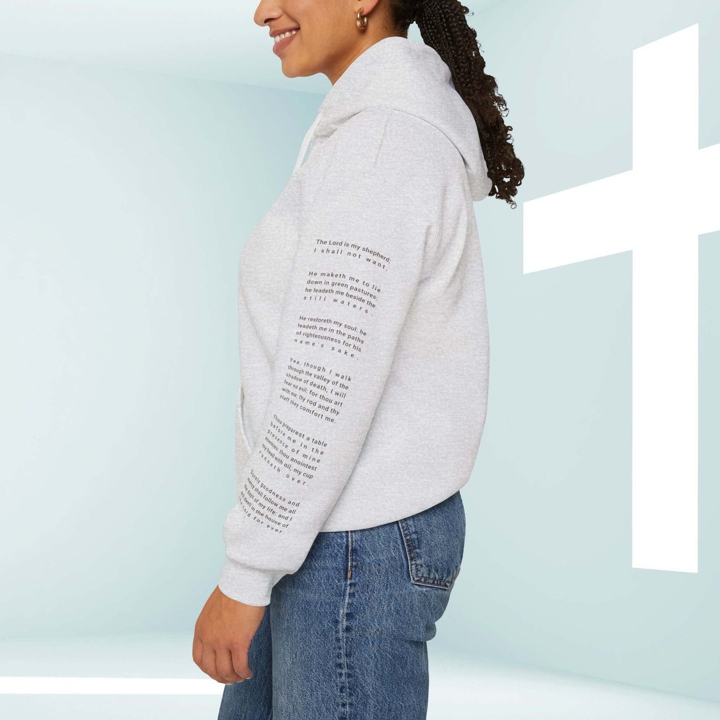 Woman wearing Fearless Psalm 23 Christian hoodie with religious text on the sleeve, standing beside a white cross in a serene background.