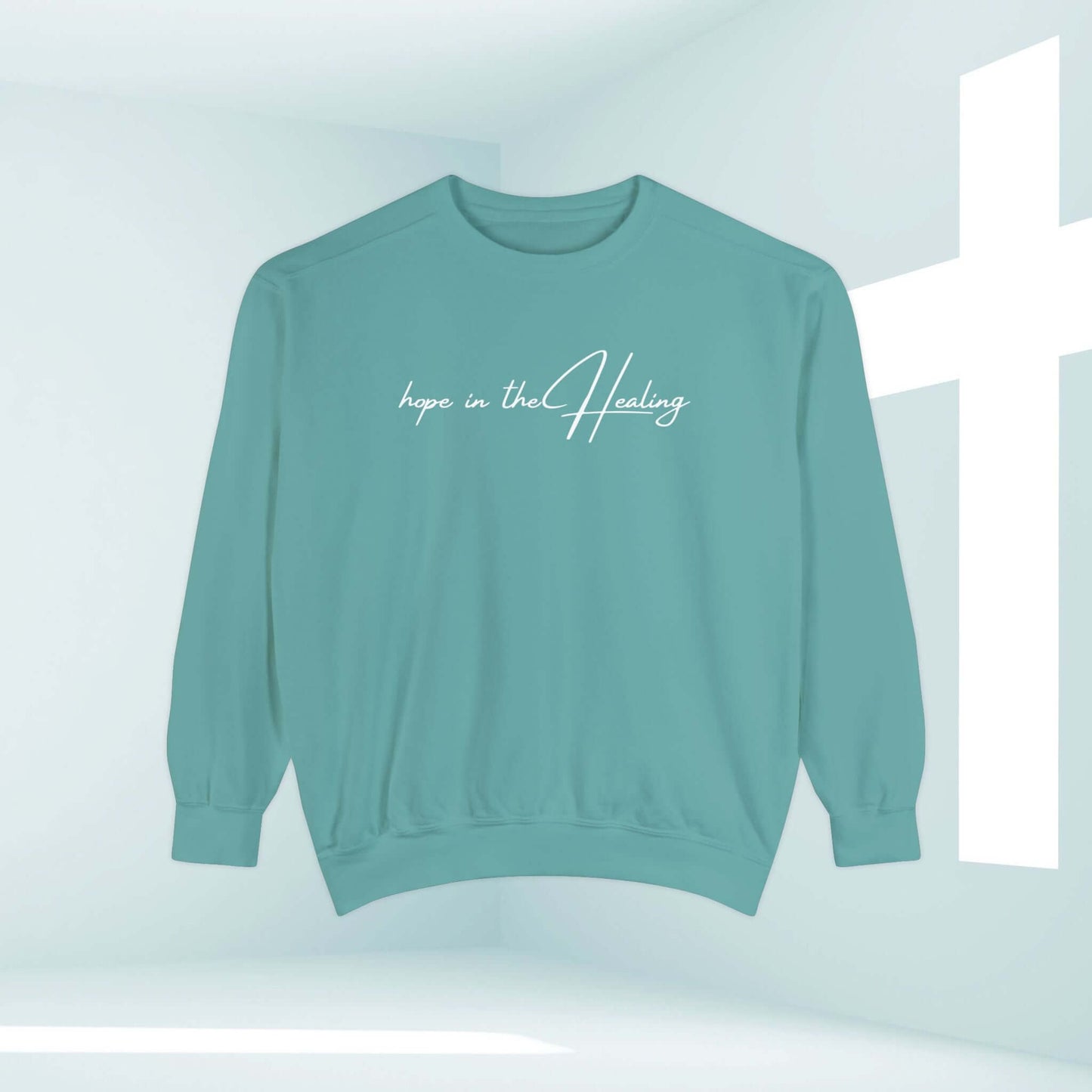 Hope In The Healing Christian sweatshirt crewneck in teal with biblical message displayed against a serene white background with cross.