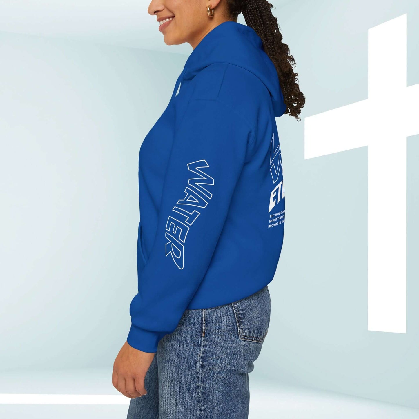 Side view of a person wearing a blue Living Water Eternal Life Christian hoodie with Bible verse graphics, standing by a white cross.