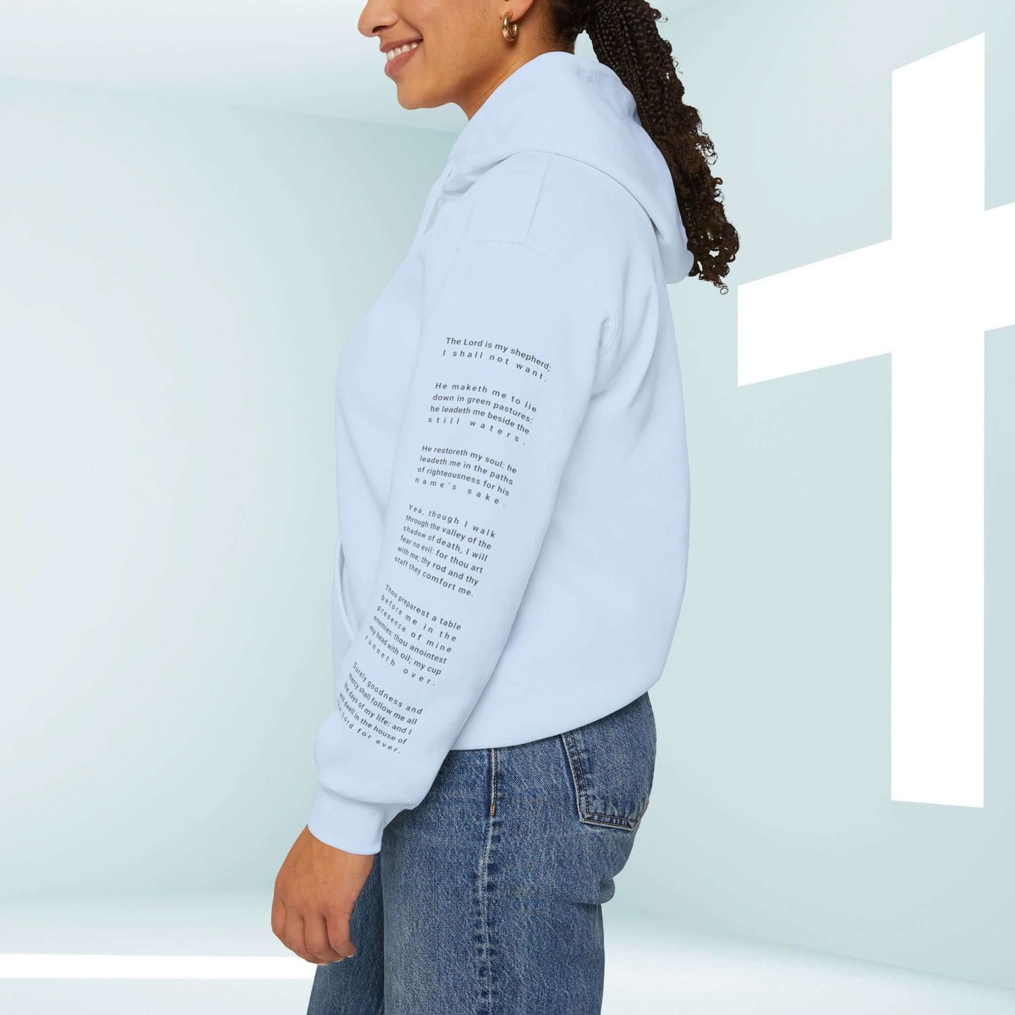 Woman wearing Fearless Psalm 23 No Fear Christian Hoodie showcasing scripture graphic on the sleeve in front of a white cross backdrop