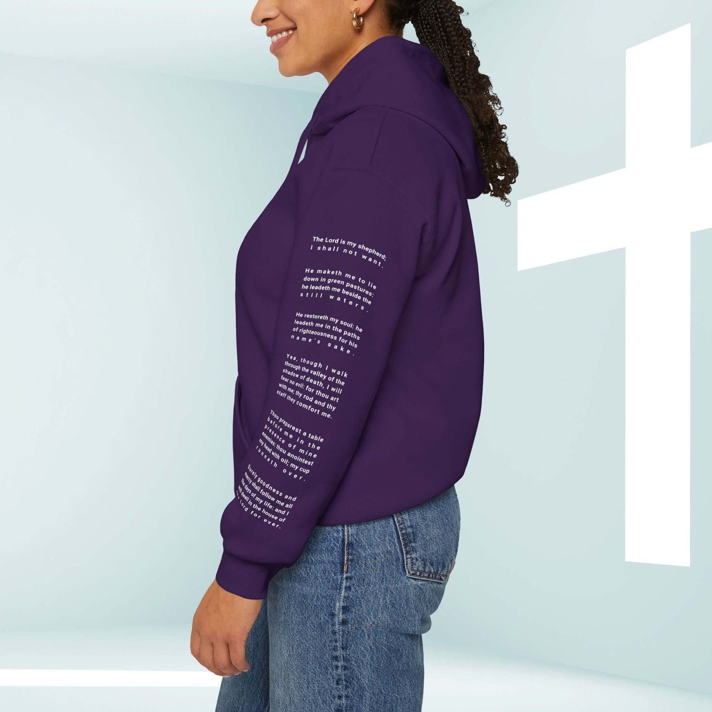 Woman wearing purple Fearless Psalm 23 Christian hoodie with Bible verse graphics on sleeve, standing by a white cross.