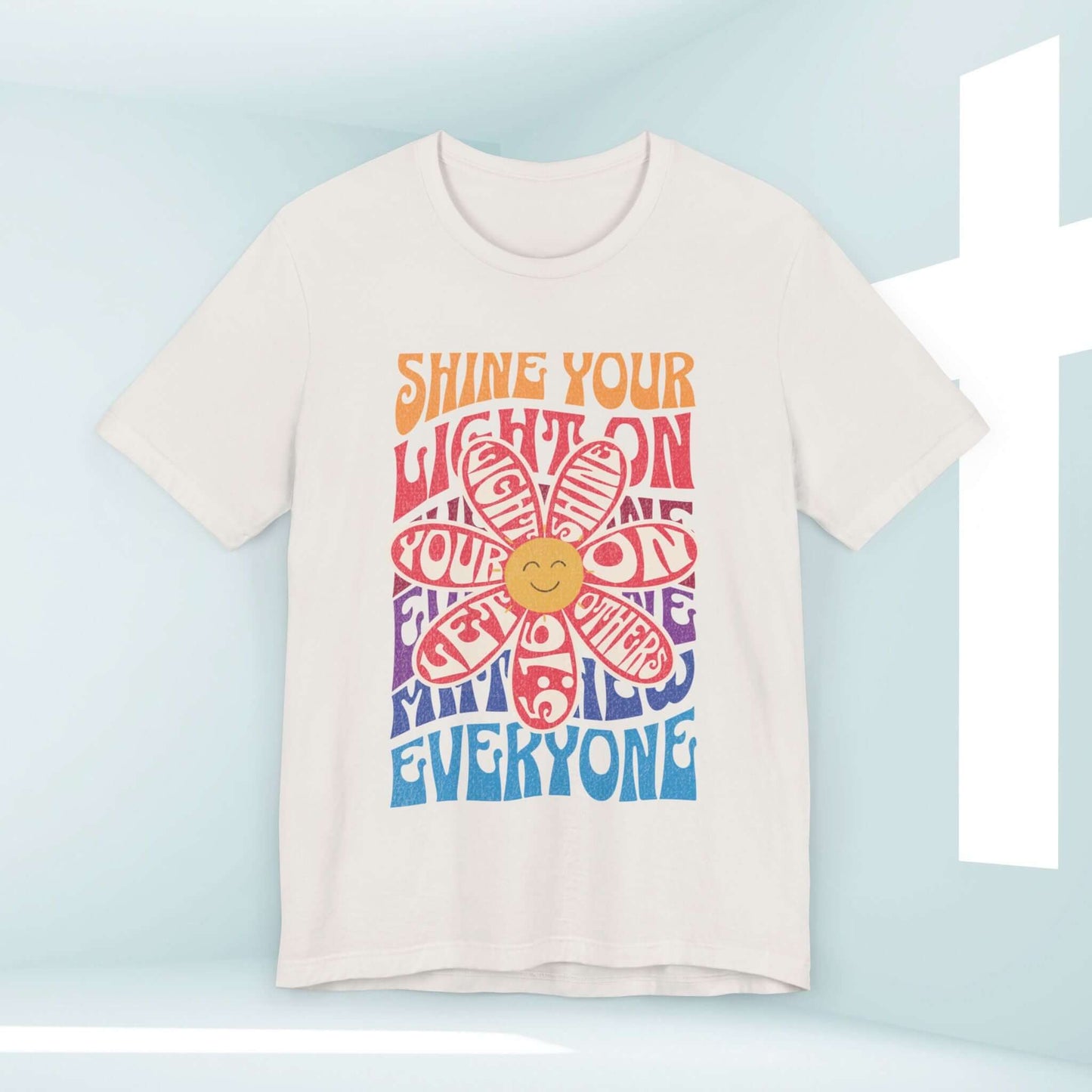 Shine Your Light Christian shirt with colorful retro design and positive message on a white tee in a light background.