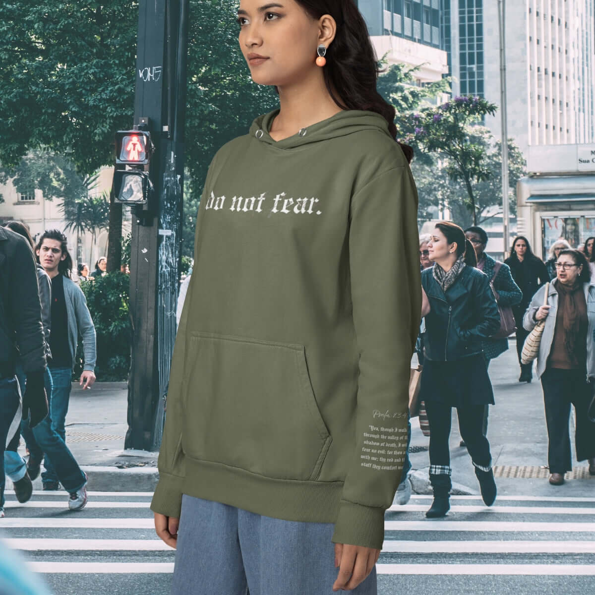 Woman wearing a green Christian hoodie with Bible verse text on the sleeve, standing next to a white cross.