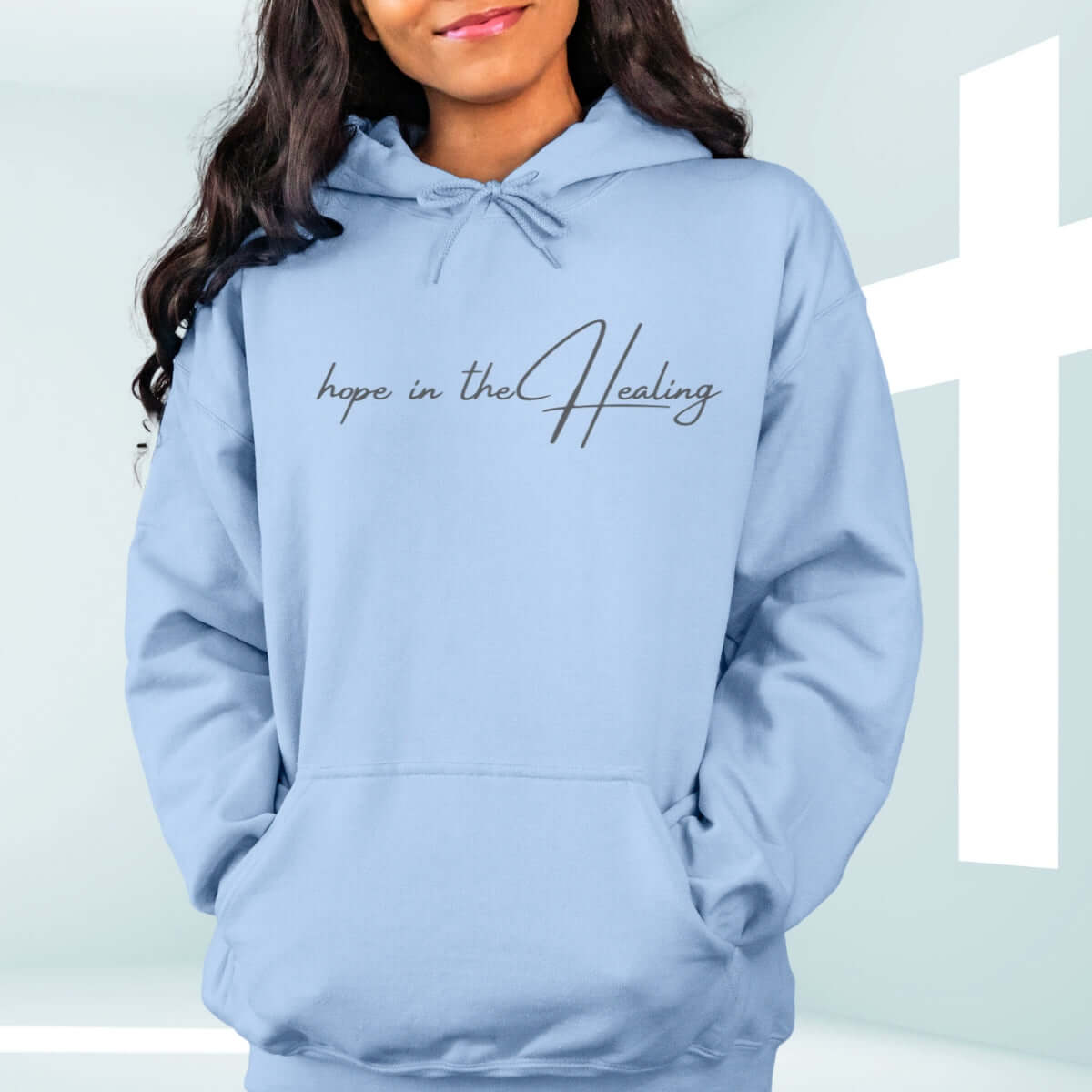 Light blue Christian hoodie with "Hope in the Healing" text displayed on wooden background with flowers