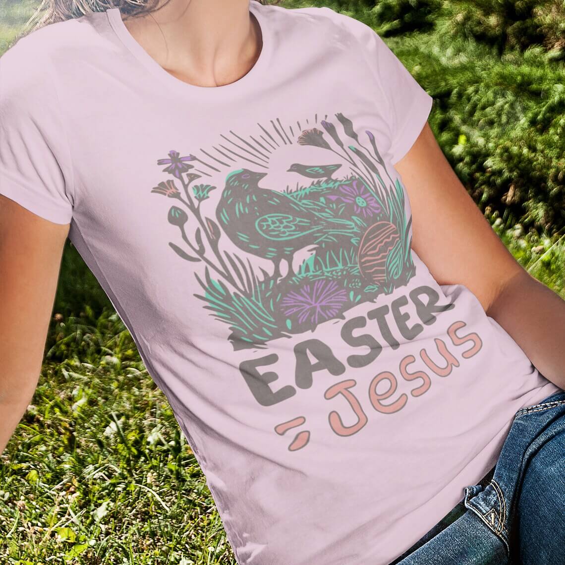 Woman wearing a pink "Easter Equals Jesus" Christian Easter t-shirt with faith-based graphic design, sitting outdoors on grass