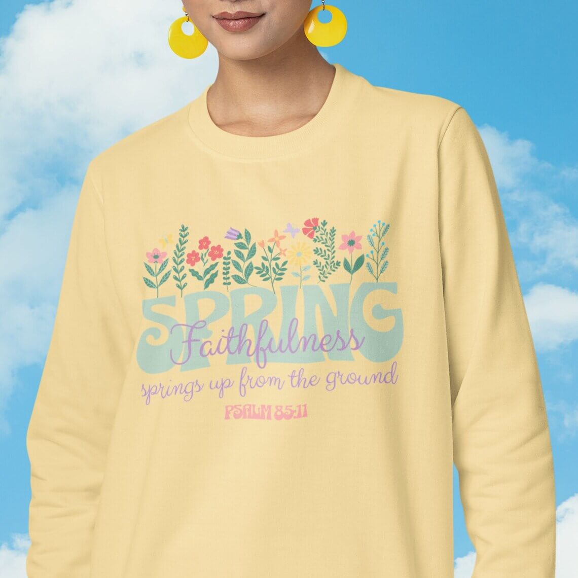 Floral Christian sweatshirt with Bible verse, "Faithfulness springs up from the ground" and colorful flowers design against blue sky.