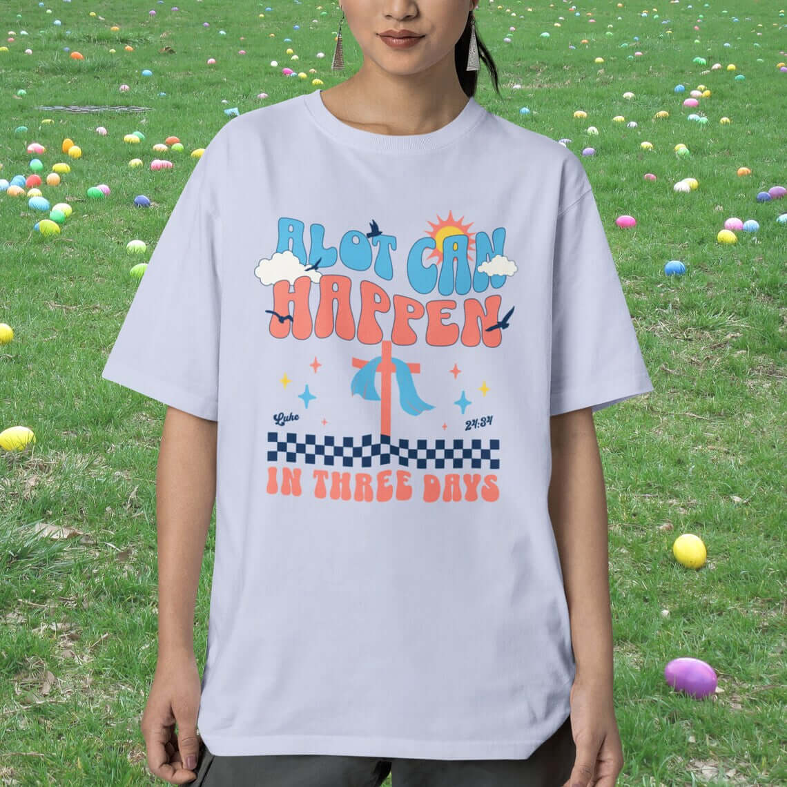 Christian Easter shirt with "Alot Can Happen In Three Days" design worn by person in field with Easter eggs